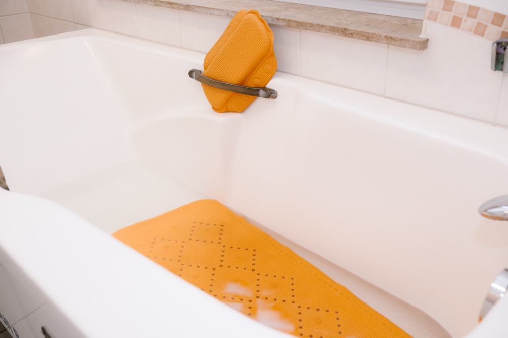 Badewanne mit orangefarbener Badematte und Nackenkissen
